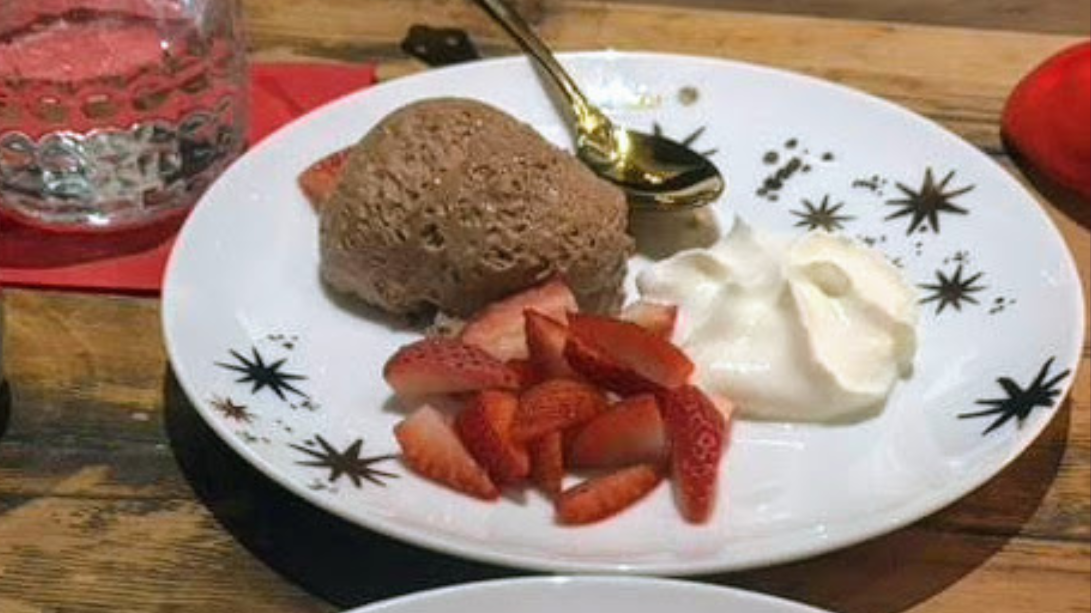 Cafe D'Anvers' chocolate mousse on a white plate with a side of strawberries and whipped cream.